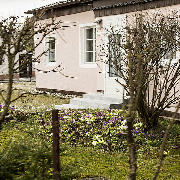 Ein kleiner Garten mit einem einstöckigem rosa Wohnhaus.