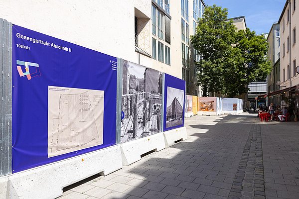 Blick in eine verkehrsberuhigte Straße, begrenzt durch Bauzaunelemente auf der linken Seite.