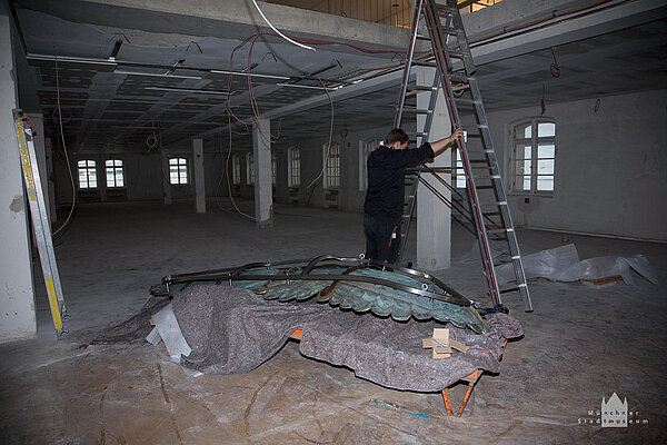 Baustelle in einem zukünftigen Ausstellungsraum mit Arbeiter, der eine Leiter aufstellt.