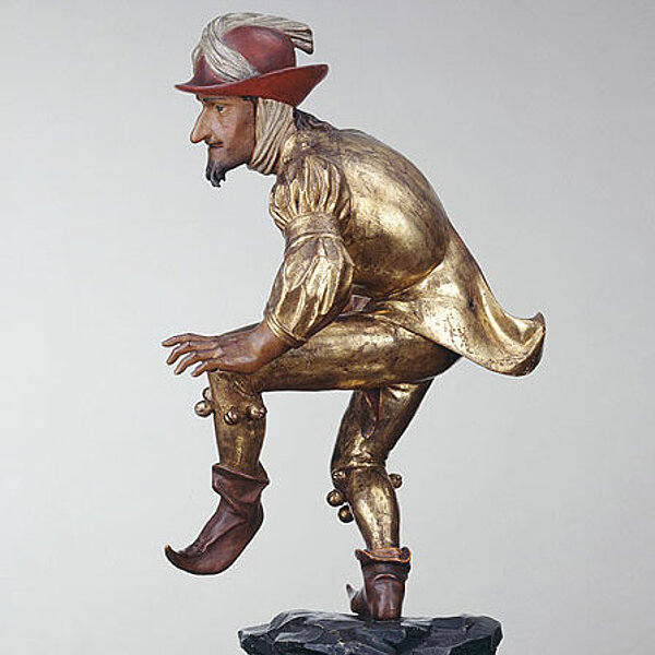 Tanzende männliche Holzfigur, überwiegend in gold und rot bemalt.