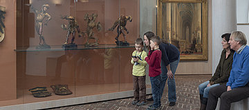 Eine Familie betrachtet historische Holzfiguren in einem Ausstellungsraum.