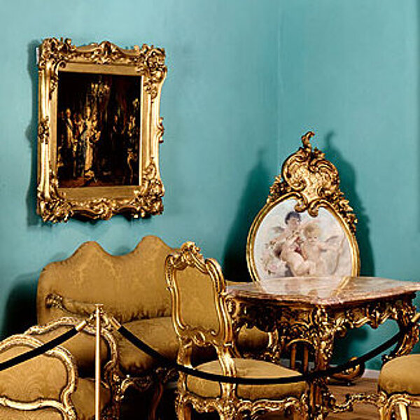 Detailansicht eines historischen Arrangements einer Historisches Arrangement einer prunkvollen Wohnzimmermöblierung mit viel Gold und hellblauer Wandfarbe.Wohnzimmermöblierung mit viel Gold und hellblauer Wandfarbe.