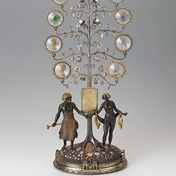 Filigran verzierte Metallskulptur eines stilisierten Baums mit einer weiblichen und einer männlichen Figur.
