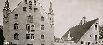 historische Schwarzweiß-Fotografie einer mehrstöckigen Gebäudefassade und Nebengebäude.