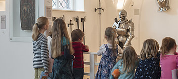 Kinder in einem Ausstellungsraum mit Ritterrüstung.