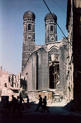 zerstörte Kirche von hinten mit beiden noch stehenden Türmen, im Vordergrund schemenhaft 6 Personen zu sehen