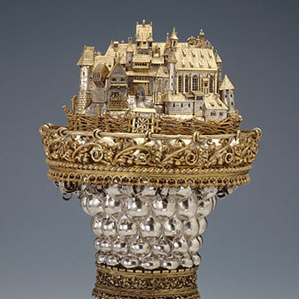 Reich verzierter gold-silbener Pokal mit einer Darstellung  eines burgartigen Gebäudekomplexes auf dem Deckel.