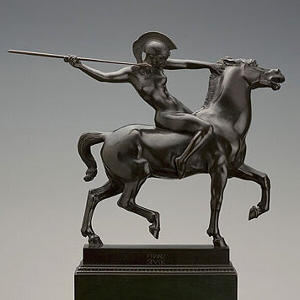 gegossene Skulptur einer zum Angriff bereiten Reiterin mit Pferd und Sper auf einem Sockel.