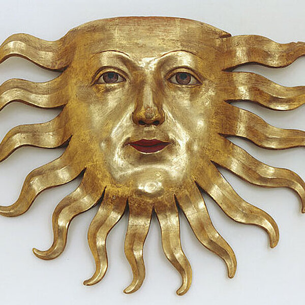 Sonne aus Holz mit Gesicht, golden bemalt.