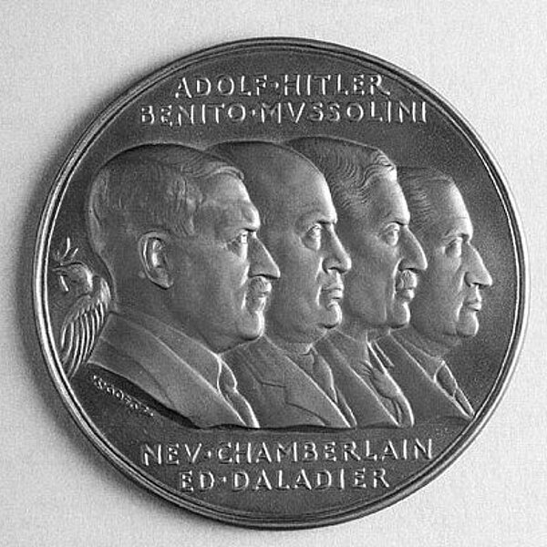 Silberne Münze geprägt mit vier Männerprofilen und vier Namen (Adolf Hitler, Benito Mussolino, Nev Chamberlain, Ed Daladier).