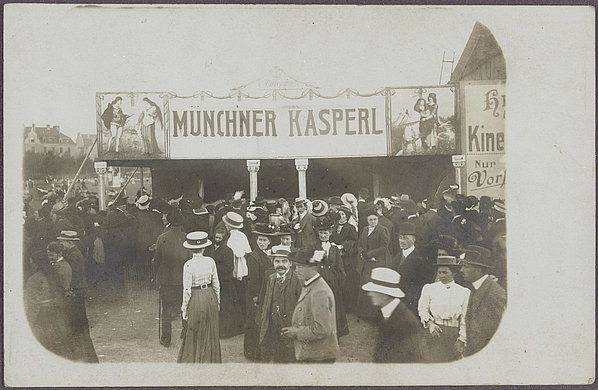 Schwarz-Weiß-Fotografie von Menschen vor der Kasperbude auf dem Oktoberfest