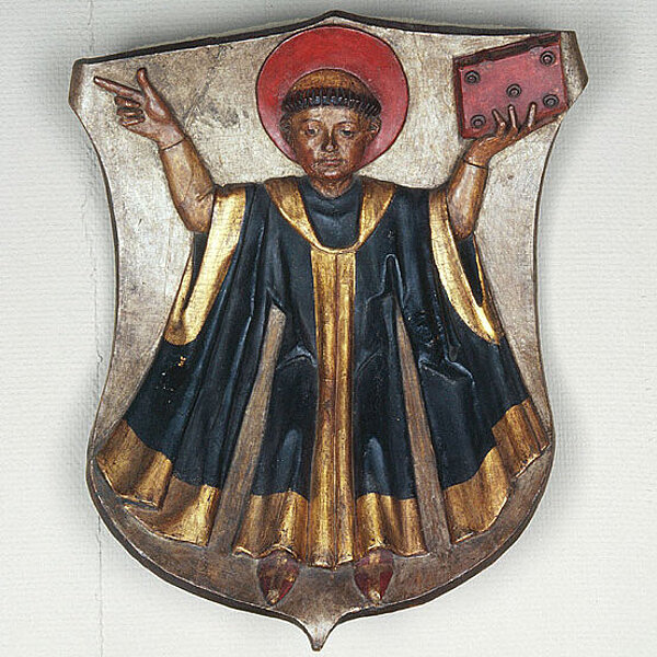 geschnitztes Stadtwappen mit Mönch in schwarz goldener Kutte mit rotem Buch in der Hand.